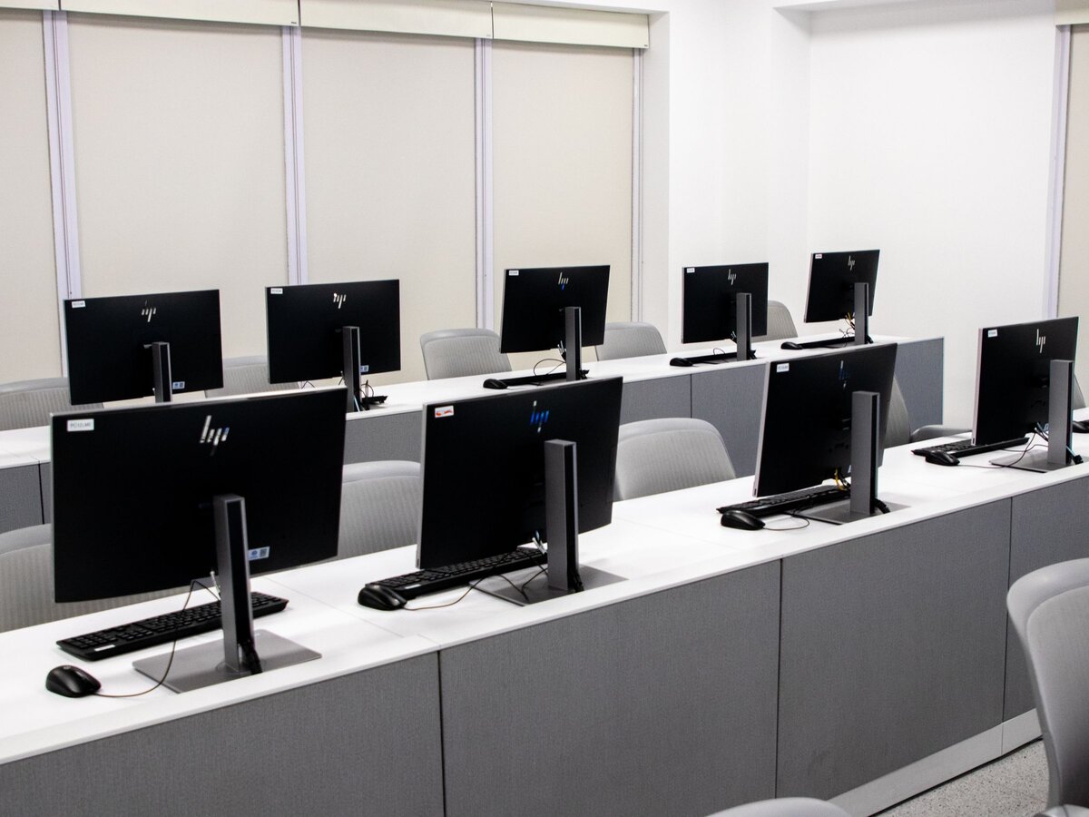 An empty school computer lab, rows of identical monitors waiting on the desks before students arrive